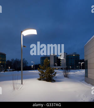 Street lamps of the office buildings. Lighting supports and lamps. Winter, snow, evening. Stock Photo