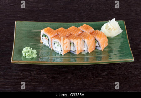 Sushi rolls on a plate with salmon on dark brown wooden table. Side view. Stock Photo