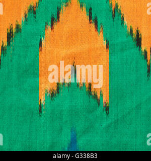 Uzbek silk atlas Ikat. Orange, green and blue ornament. Close up fragment of the top view. Stock Photo