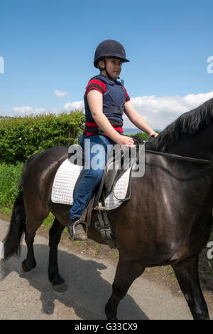 Young girl riding a dark bay horse on a sunny summer day. Wearing a hat and body protector. Stock Photo