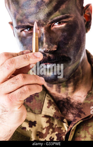 a marksman or sharpshooter wearing army camouflage face paint and holding a bullet isolated over a white background Stock Photo