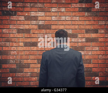 A business man has his back turned and looking at a brick wall. Can represent an obstacle, sadness or a struggle. Stock Photo