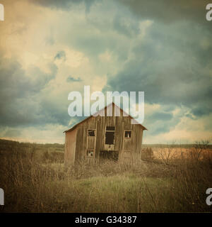 An old abandoned farm house is in the country with scary clouds in a field for a destruction, barn or scary concept. Stock Photo