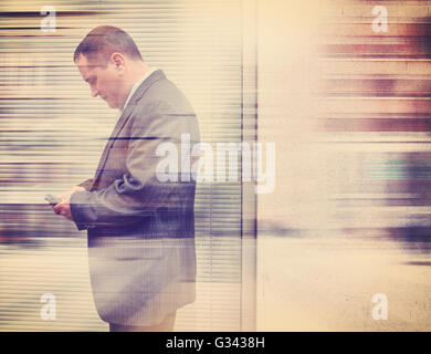 A business man in a suit is texting on his cell phone in the city outside with a wall for a communication or message concept. Stock Photo