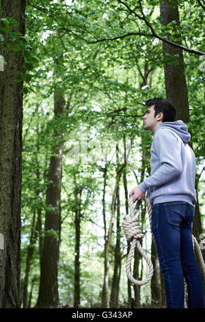 Depressed Man Contemplating Suicide By Hanging In Forest Stock Photo