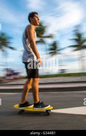 RIO DE JANEIRO - MARCH 6, 2016: Young carioca Brazilian man on skateboard moves in a motion blur along the beachfront street. Stock Photo