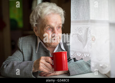 Elderly woman drinking tea sitting at the table. Stock Photo