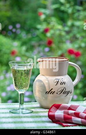 Vin du Pays table wine jug and glass of French country white wine on sunlit vacation alfresco terrace table with floral garden behind Gites de France Stock Photo