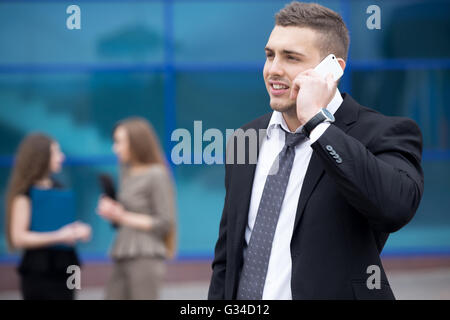 Portrait of confident young business man looking sideways while talking on smartphone outdoor. Successful attractive man using Stock Photo