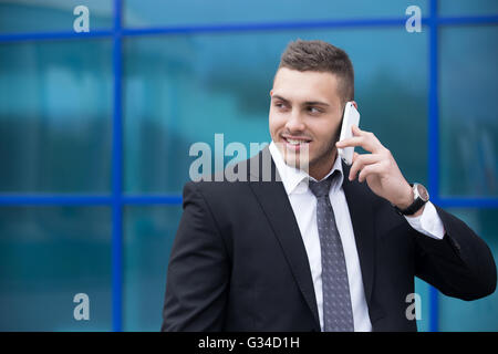 Portrait of cheerful young man looking sideways while talking on smartphone outdoors. Happy handsome caucasian man using mobile Stock Photo
