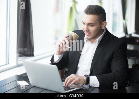 Portrait of confident happy smiling young business man sitting with glass of drink in coffee shop interior. Successful Stock Photo