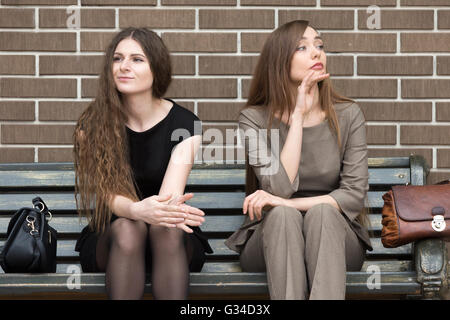 Full length portrait of two beautiful young female rivals sitting side by side on bench. Attractive caucasian office women Stock Photo