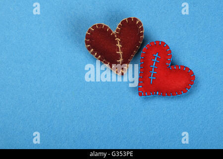 Felt craft and art, two handmade stitched toy hearts, red and brown together on blue background Stock Photo