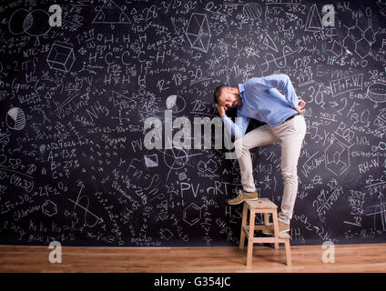 Man at step ladder, against big blackboard, formulas, symbols Stock Photo