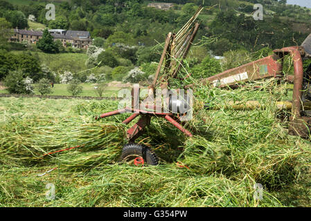 Farm machinery spinning grass in a hay meadow in the English countryside. Stock Photo