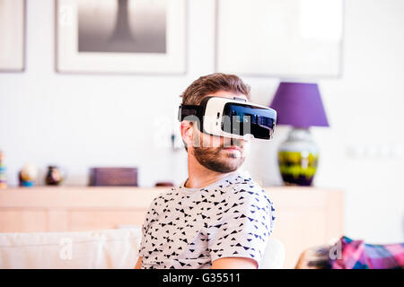 Man wearing virtual reality goggles, sitting in living room Stock Photo