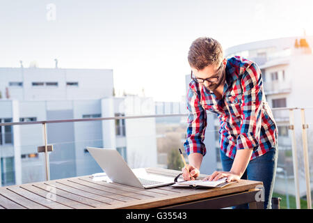 Businessman working from home on laptop, standing on balcony Stock Photo