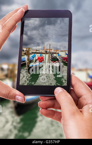 a woman using a smart phone to take a photo of some gondolas moored in Venice, Italy Stock Photo