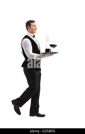 Full length profile shot of a young waiter carrying a tray with wine and two glasses isolated on white background Stock Photo