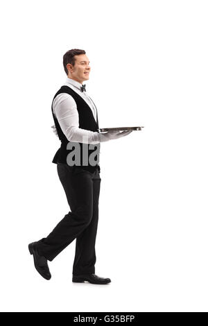 Full length profile shot of a young waiter walking with an empty tray isolated on white background Stock Photo