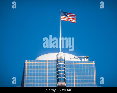 American flag waving on top of a modern skyscraper high in the air on a sunny day against the blue sky Stock Photo