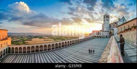 Famous Basilica of St. Francis of Assisi (Basilica Papale di San Francesco) with monk and Lower Plaza at sunset in Assisi, Umbri Stock Photo