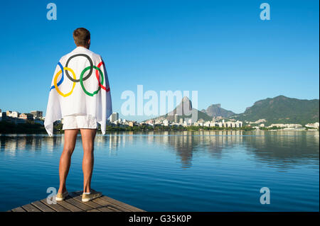 RIO DE JANEIRO - MARCH 27, 2016: Athlete stands draped in Olympic flag at Lagoa Rodrigo da Freitas Lagoon, a Games venue. Stock Photo