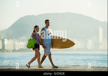 RIO DE JANEIRO - APRIL 5, 2016: A young Brazilian surfer couple walks along the beachfront boardwalk at Copacabana. Stock Photo