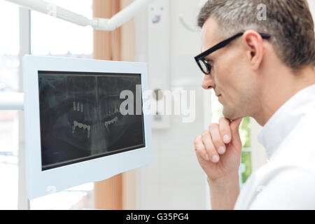 Male dentist looking teeth on digital X-Ray computer monitor wering glasses Stock Photo