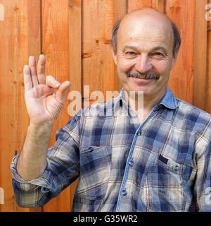 elderly man in a plaid shirt, bald, with a mustache shows sign okay. Approval and positive recommendations Stock Photo