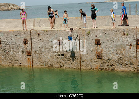 Boys and girls jumping from the jetty into the sea at the harbour in Herm Island, Channel Island Stock Photo