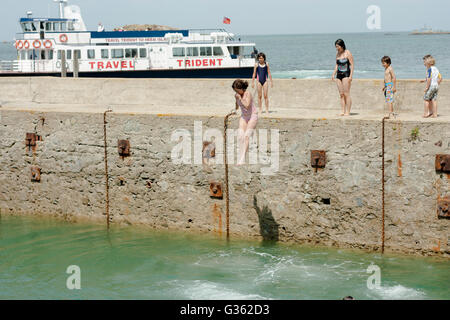 Boys and girls jumping from the jetty into the sea at the harbour in Herm Island, Channel Island Stock Photo