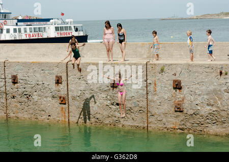 Boys and girls jumping from the jetty into the sea at the harbour in Herm Island, Channel Island Stock Photo