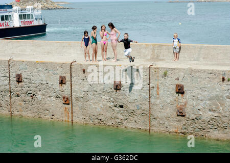 Boys and girls jumping from the jetty into the sea at the harbour in Herm Island, Channel Island Stock Photo