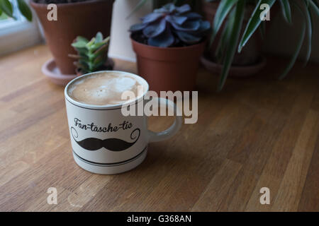 A cup of fresh coffee on a worksurface near some succulent plants Stock Photo