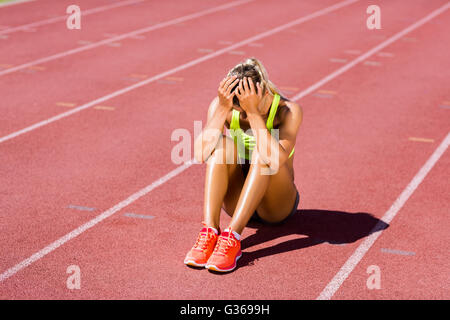 Upset female athlete sitting on running track Stock Photo