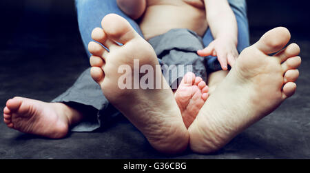 feet of a young mother and her baby, wearing jeans and sitting on the floor Stock Photo