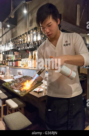 Waiter cooks fresh meat with a blow-torch in a restaurant in Kabukicho, Tokyo, Japan Stock Photo