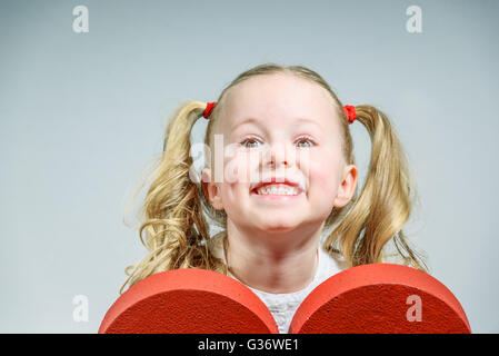 Beautiful smiling blond girl in a school uniform with a big red heart on Valentine's Day. Stock Photo
