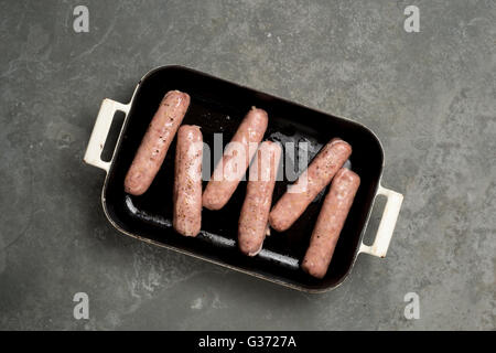 Raw sausages in a cast iron pan, sprinkled with pepper on a grey slate background Stock Photo