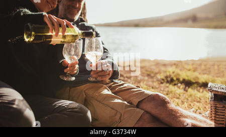 Cropped image of woman pouring wine in glasses. Couple camping near a lake enjoying with a glass of wine, focus on wine glasses. Stock Photo