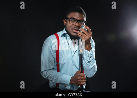 Stylish afro amerian man singing into vintage microphone over dark background Stock Photo