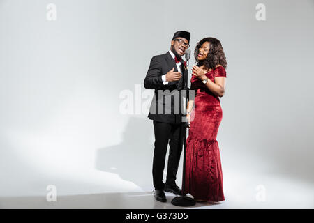 Full length portrait of afro amerian couple singing into vintage microphone over dark background Stock Photo