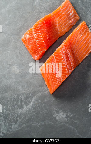Two fillets of raw trout on a grey slate surface shot overhead with copy space Stock Photo