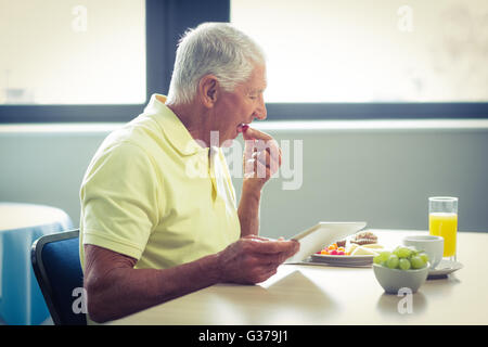 Senior man using digital tablet while having breakfast Stock Photo