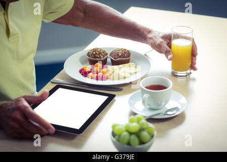 Senior man using digital tablet while having breakfast Stock Photo