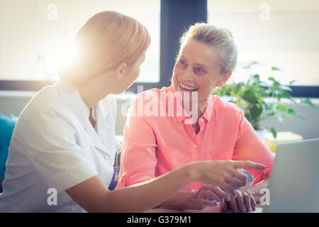 Female nurse and senior woman smiling while using laptop Stock Photo