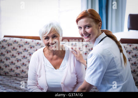 Portrait of smiling senior woman and female doctor in living room Stock Photo