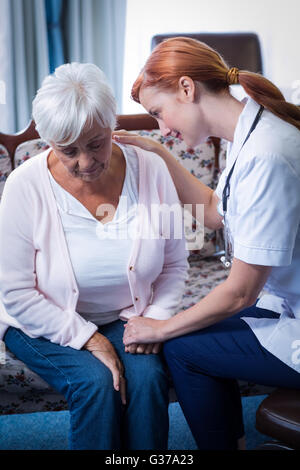 Female doctor consoling senior woman in living room Stock Photo