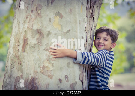 Smiling boy hugging tree trunk in park Stock Photo